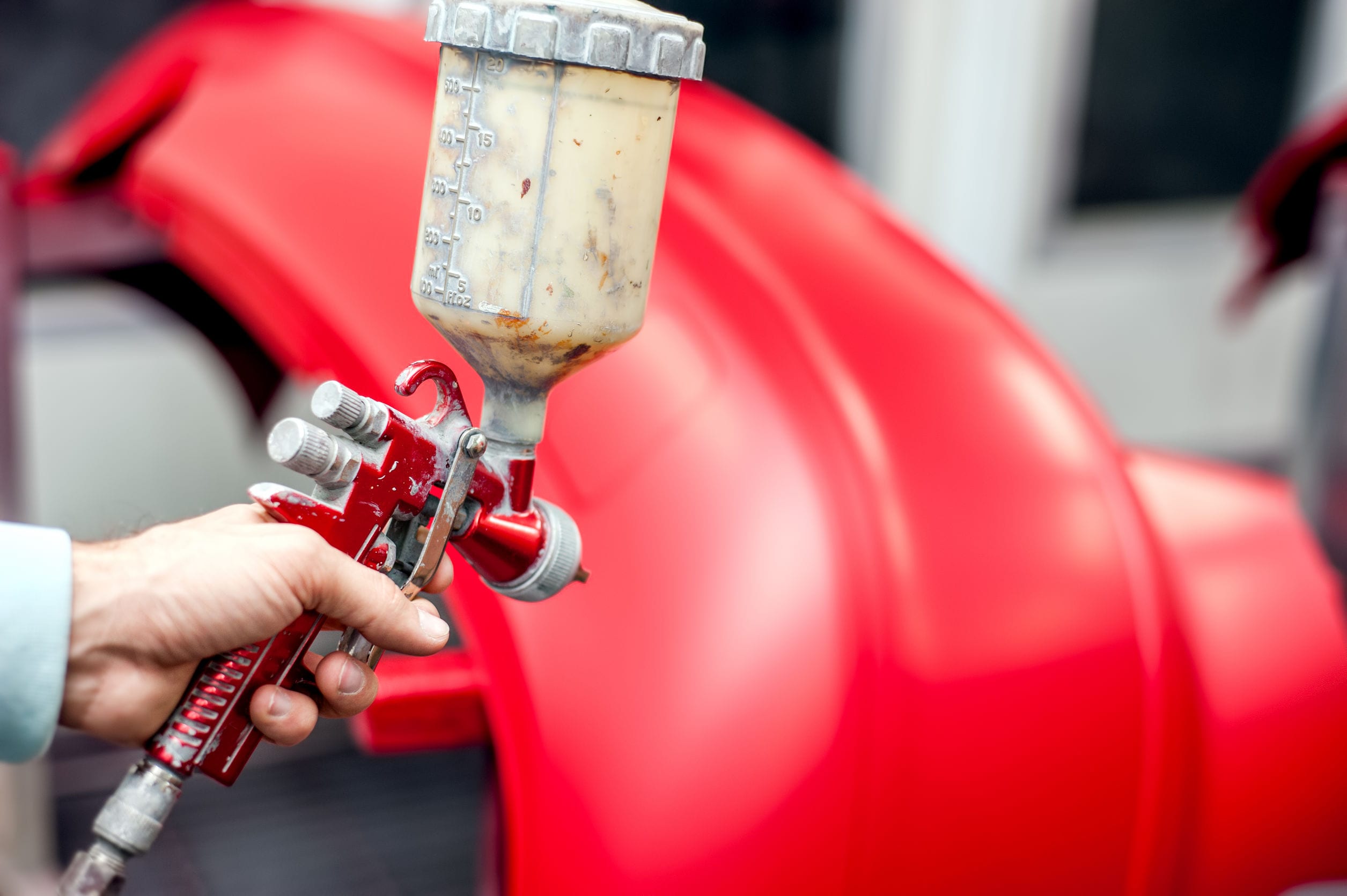 Close-up of spray gun with red paint painting a car in special b Close-up of spray gun with red paint painting a car in special booth